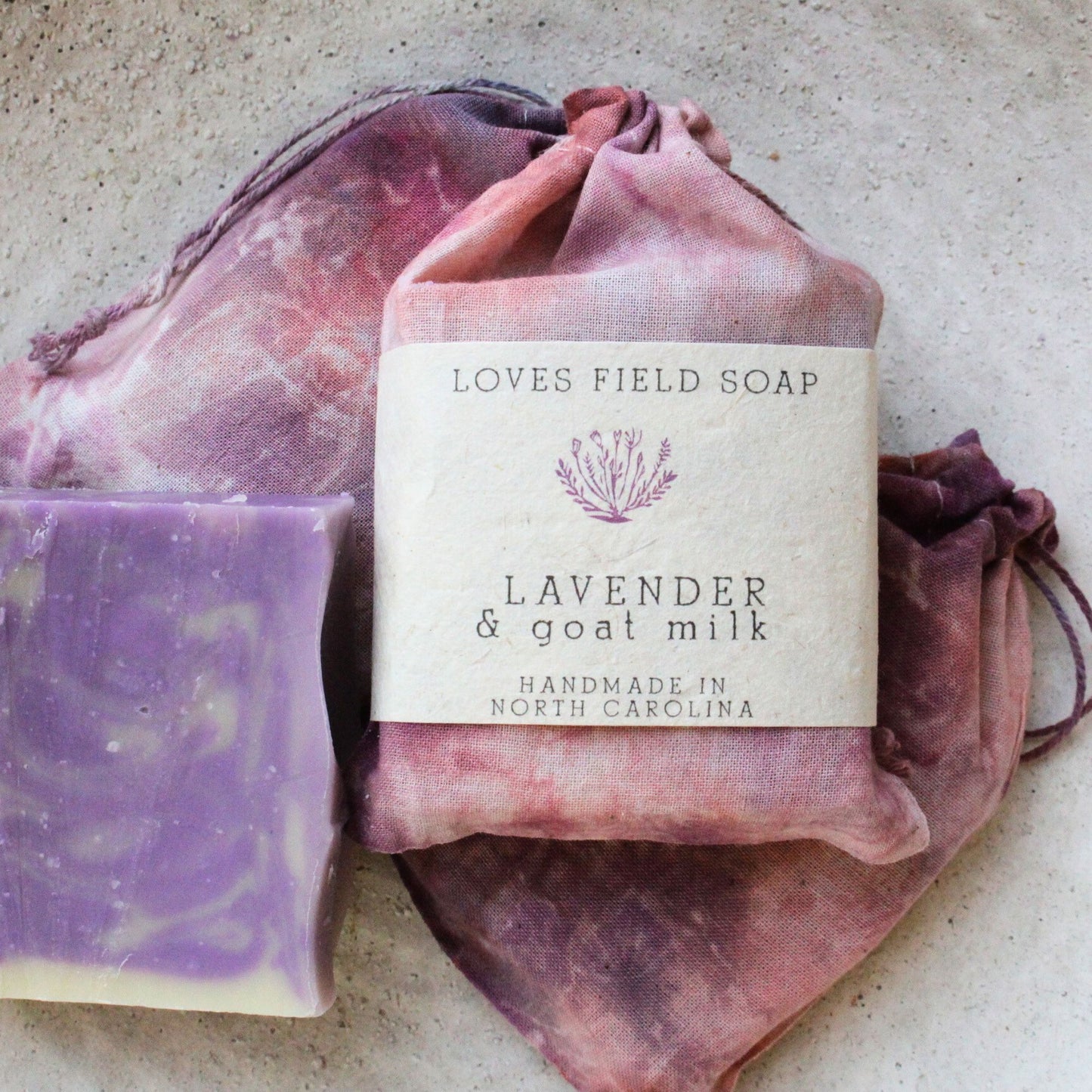 Bar of lavender soap with goat milk on a pink drawstring bag, branded 'Loves Field Soap'.