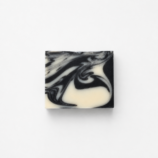 Fragrance-free charcoal and clay goat milk soap bar with black and white swirls on white background