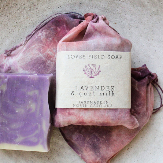 Bar of lavender soap with goat milk on a pink drawstring bag, branded 'Loves Field Soap'.