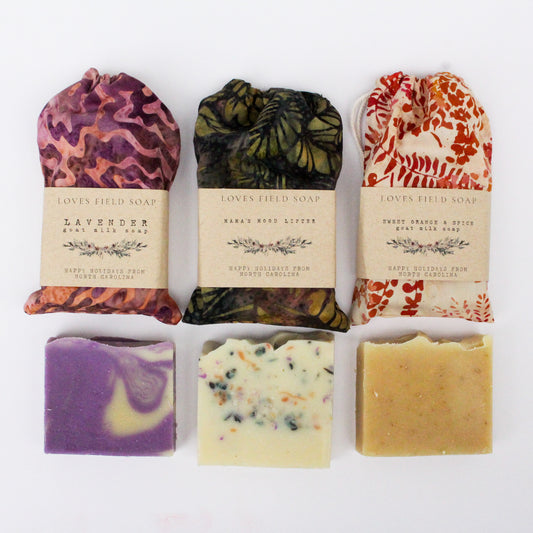 handmade soap gift set with three natural soap bars, one purple in colorful cotton drawstring bag one speckled colors and one beige