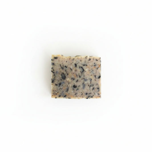 A rectangular bar of cedarwood handmade soap with black speckled soap pieces, sitting on a white surface.