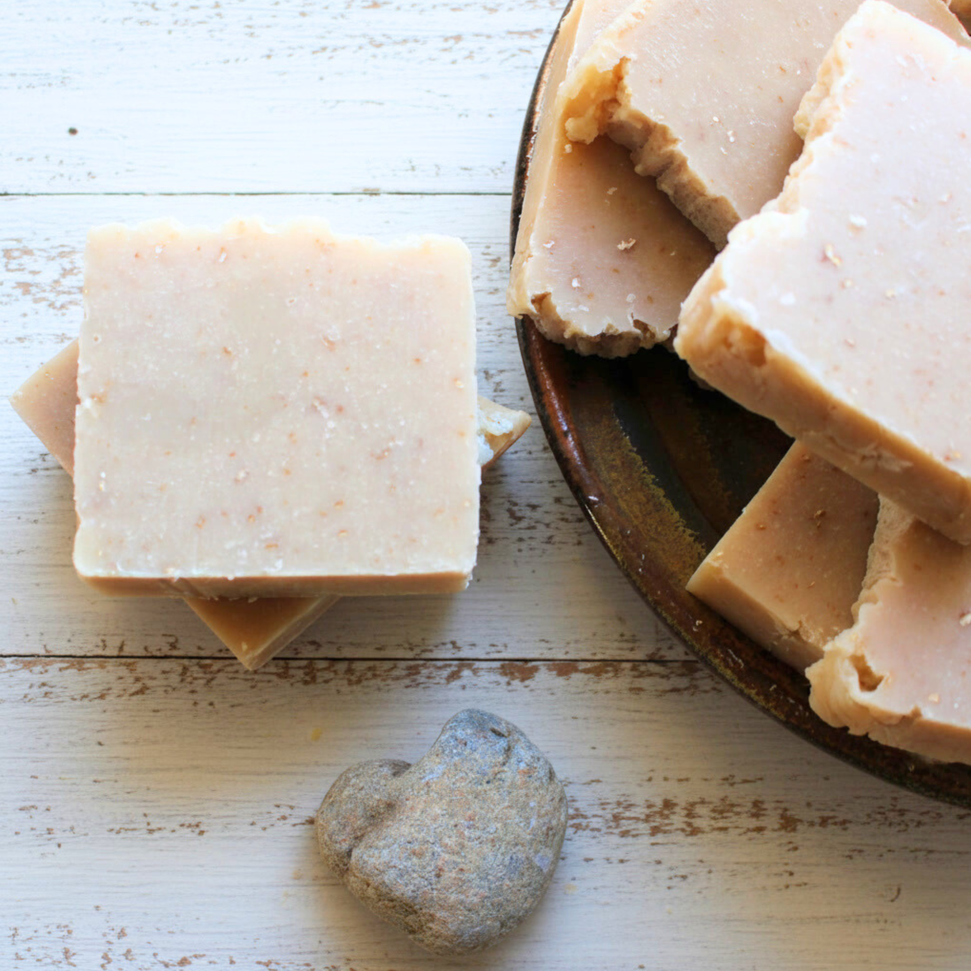 Three bars of soap on a wooden surface with a heart-shaped bar of soap.
