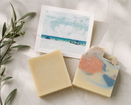 Two bars of soap with a beach scene art card on a light fabric background