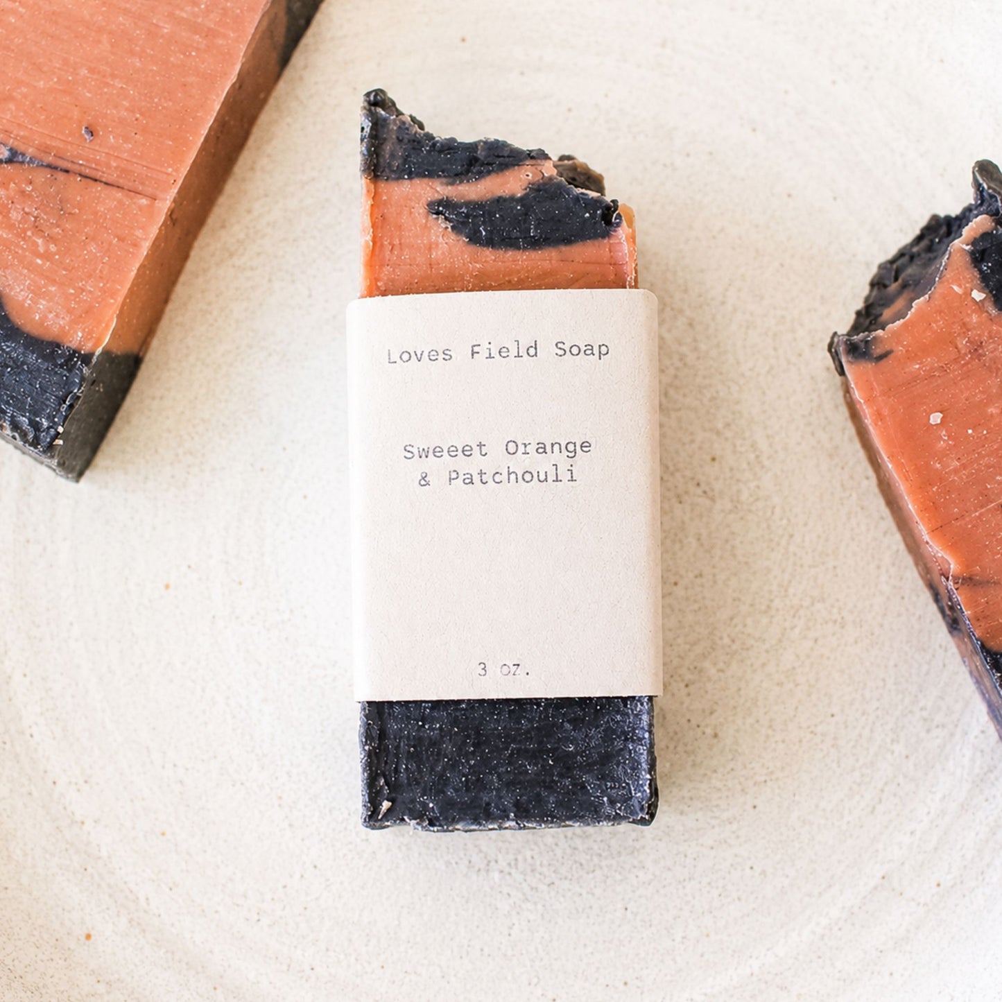 deep clay red and charcoal soap wrapped in light brown label that says sweet orange and patchouli soap