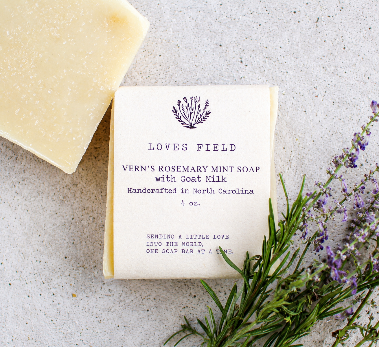 Bar of soap with a label on a concrete surface with lavender and rosemary.